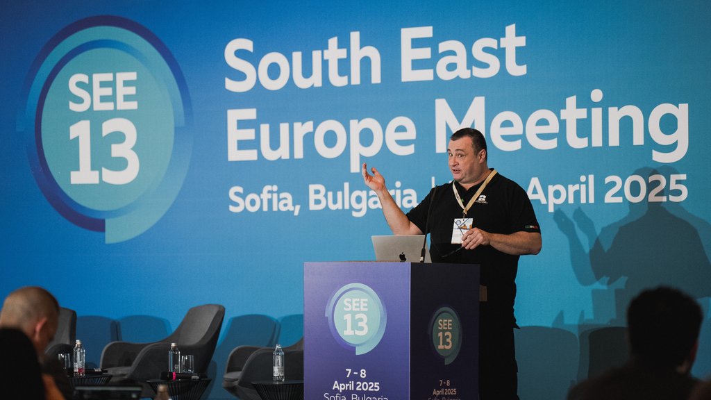 A white man in a black t shirt presents on stage.